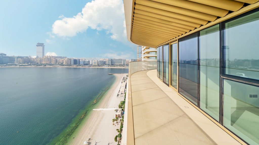 Spacious balcony view of coastal city skyline and sandy beach under a clear blue sky.