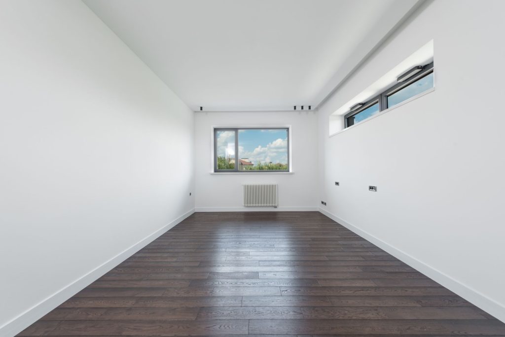 Interior of empty spacious room with white walls and brawn parquet floor in daylight