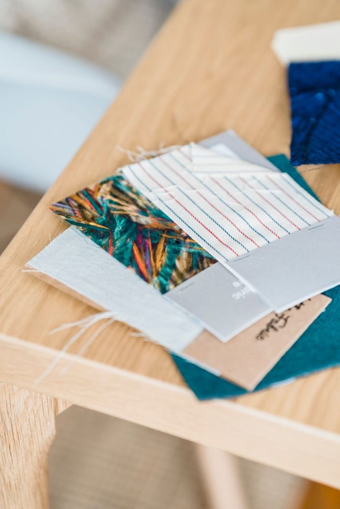 From above samples of colorful textile with patterns placed on wooden table in light room on blurred background in workshop